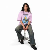 Model seated on a stool in the Ash Lilac oversized tee, full length